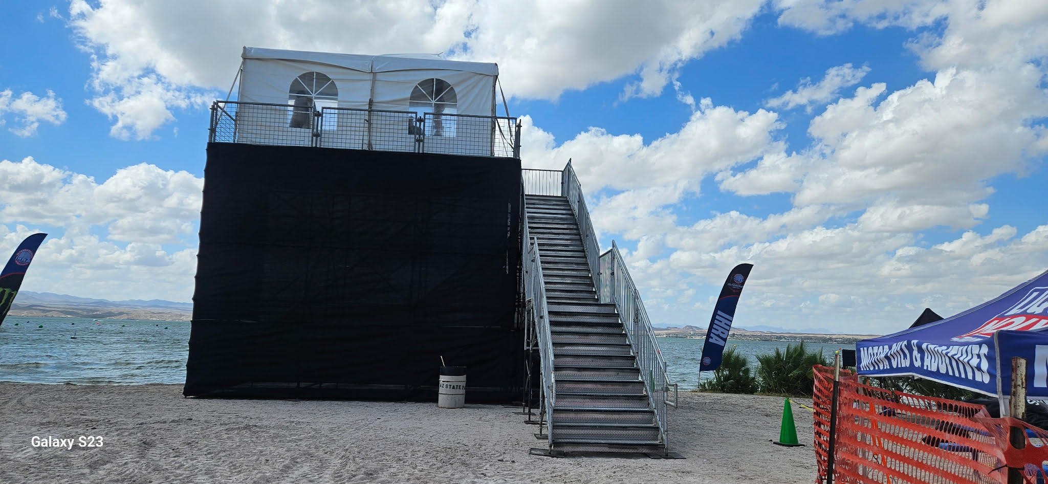 Elevated event platform with a wide exterior staircase beside a lake
